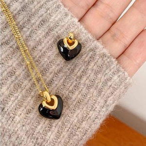 Détail d'un collier pendentif cœur noir avec chaîne dorée sur fond de pull gris