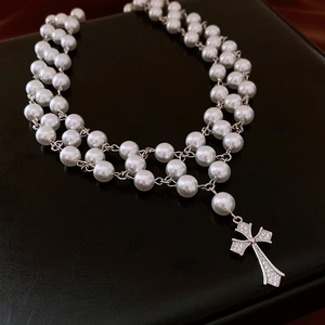 Detail of double-layer pearl necklace with a sparkling zircon cross pendant on black leather