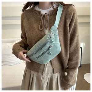 Light green corduroy waist bag with adjustable strap and triangular zippers on crossbody strap