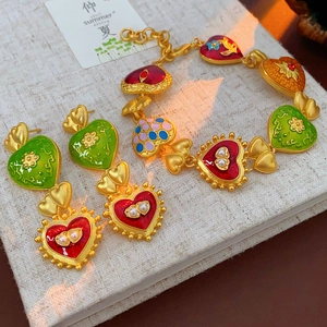 Detail of vintage heart jewelry set with colorful enamel and pearls on a textured journal