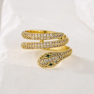 Snake wrap ring in gold finish with white zircons and green gem eyes on stone background
