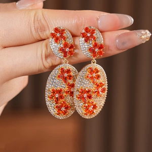 Detailed close-up of vintage gold flower earrings with orange crystals held in hand