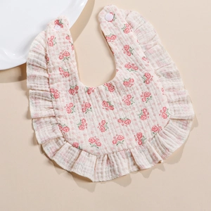 Detail of baby muslin bib featuring pink rose print, ruffled edges and snap buttons