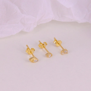 Detail of three gold star and moon earrings with clear gems on pink paper