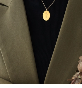 Detail of a gold oval pendant necklace with flower engraving worn on a green blazer