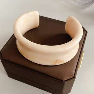 Detail of a wide marble-patterned resin cuff bracelet on a brown silk gift box