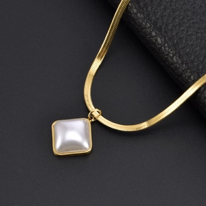 Detail of gold snake chain necklace featuring a square pearl pendant on dark background