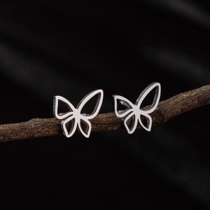 Macro shot of silver hollow butterfly stud earrings resting on a rustic branch