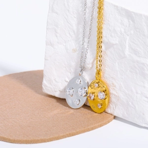 Close-up of gold and silver necklaces with oval zircon pendants on a white stone block