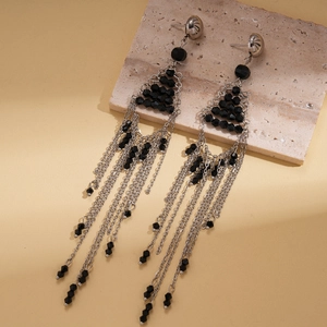 Detail of silver chain tassel earrings with black faceted glass beads on stone background