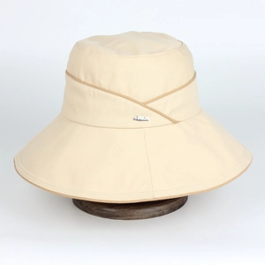 Détail d'un chapeau de soleil blanc cassé montrant la texture du coton et le logo métal