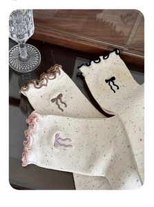 Detailed view of cream-colored mid-calf socks with ruffle trim and bow embroidery details