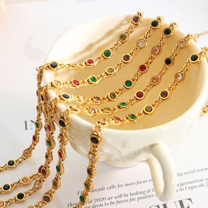 Golden necklace set with colorful zircons displayed on a white cup with fashion magazine
