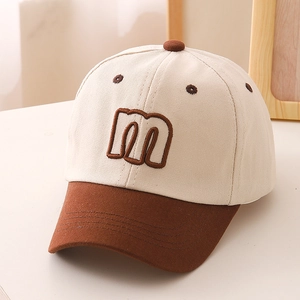 Close-up of brown embroidered letter M on beige canvas kids baseball cap brim