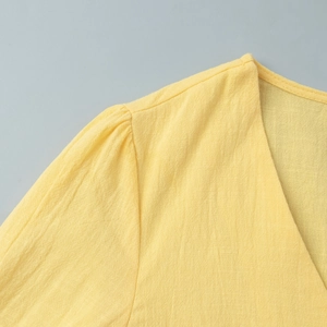 Macro detail of the bright yellow V-neck top showing textured fabric and pleated shoulders