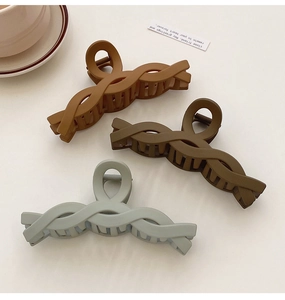 Three twisted matte hair claws in brown and grey-green on a minimal lifestyle background