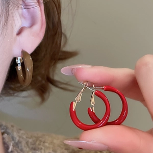 Close-up of C-shaped geometric resin drop earrings in red and brown colors