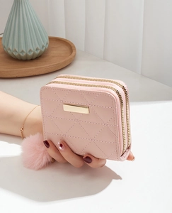 Detail of pink quilted leather wallet with dual zippers and soft pompom charm