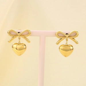 Detailed view of gold heart earrings with ribbon bow on a pink display stand