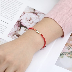 Detail of red braided rope bracelet with gold bar and small flag charm on wrist
