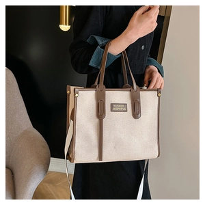 Detail of beige canvas tote bag with brown leather trim shown on a fashion model