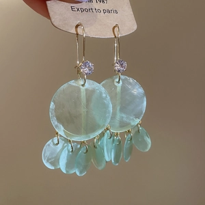 Close-up of light green translucent round shell tassel earrings with purple zircon accent