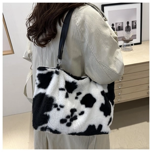 Close-up of fluffy cow print plush tote bag with black strap in a lifestyle setting