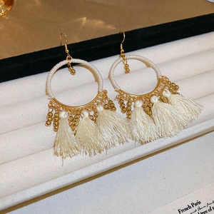 Detail view of Bohemian hoop earrings featuring off-white tassels and gold bead accents
