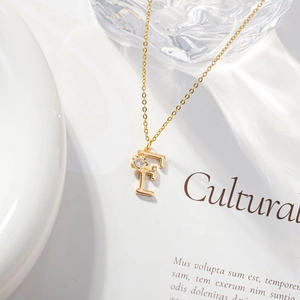 Detail shot of a golden letter F necklace with a zircon flower on an elegant white background