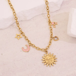Close-up of golden stainless steel necklace with sun, moon, and star charms on a beach