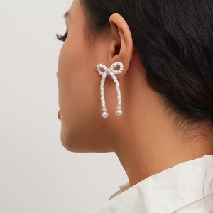 Close-up of elegant white bow earrings with imitation pearls and tassel details