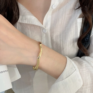 Detailed view of an 18k gold plated irregular wave bangle with a polished mirror finish