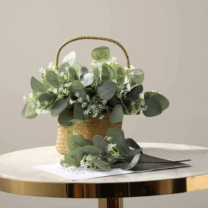 Artificial eucalyptus leaves and white flowers in a rustic woven basket on marble table