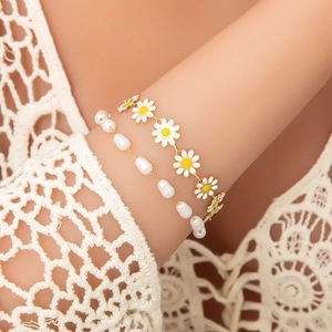 Détail d'un bracelet doré à marguerite émaillée et de perles irrégulières sur le poignet
