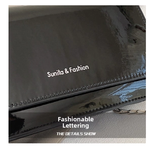 Detail of black patent leather flap bag with silver Sunita & Fashion lettering and chain