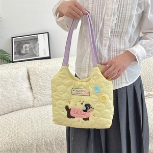 Detalle del bolso tote amarillo acolchado con bordado de perro y asas moradas