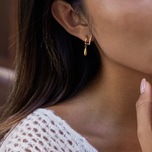Détail de boucles d'oreilles dorées asymétriques avec pendentif goutte et zircons