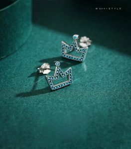 Macro shot of silver crown earrings with blue gemstones on green velvet display