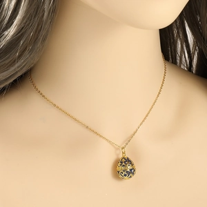 Detailed view of dark blue egg pendant with gold floral pattern on neck model