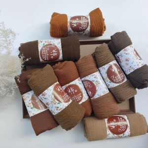 Detail of pleated cotton viscose scarves in earth tones with handcrafted paper sleeves