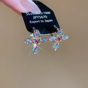 Close-up of silver hoop earrings with vibrant multi-color rhinestones in cross shape