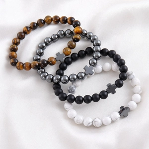 Macro shot of stone beaded bracelets with metal cross charms on white silk fabric