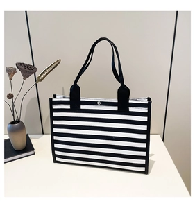 Close-up of black and white striped canvas tote bag with metal clasp on a white surface