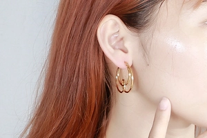 Close-up of golden geometric knotted hoop earrings worn by a model in a minimal style