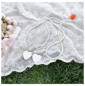 Detail of white pearl necklace featuring double heart pendants on white lace and grass