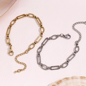 Detail of paperclip link bracelet in gold and silver finish on a soft pink background