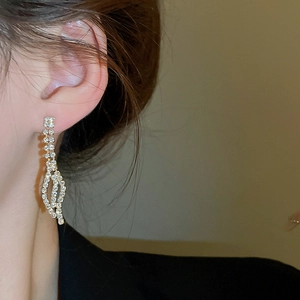 Detail shot of elegant gold leaf-shaped rhinestone earrings worn by a fashion model