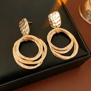 Retro gold geometric drop earrings with hammered texture on black leather background