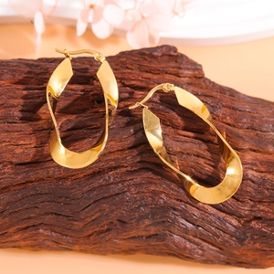 Polished 18K gold U-shaped twisted hoop earrings on natural wood base with flowers