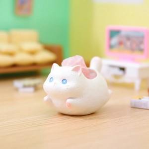 Close-up of a white resin cat figurine with a pink crystal stone on a miniature floor